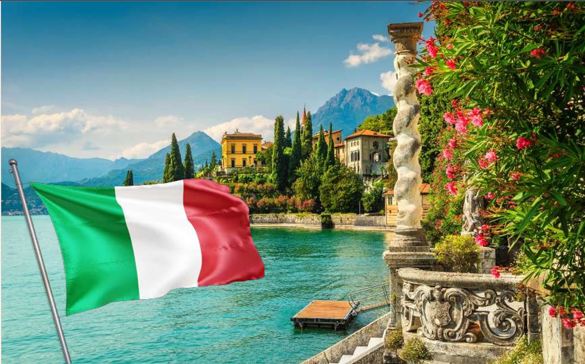Italian flag on a flagpole beside a lake with villas and mountains at Lake Como